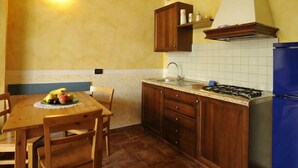 A kitchen with wooden cabinets, a gas stove, a sink, and a blue refrigerator. - Agriturismo Gian Galeazzo Visconti (Valeggio sul Mincio)