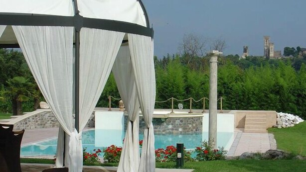 A gazebo with white drapes, a pool, and a stone wall with a statue in the background. - Agriturismo Gian Galeazzo Visconti (Valeggio sul Mincio)