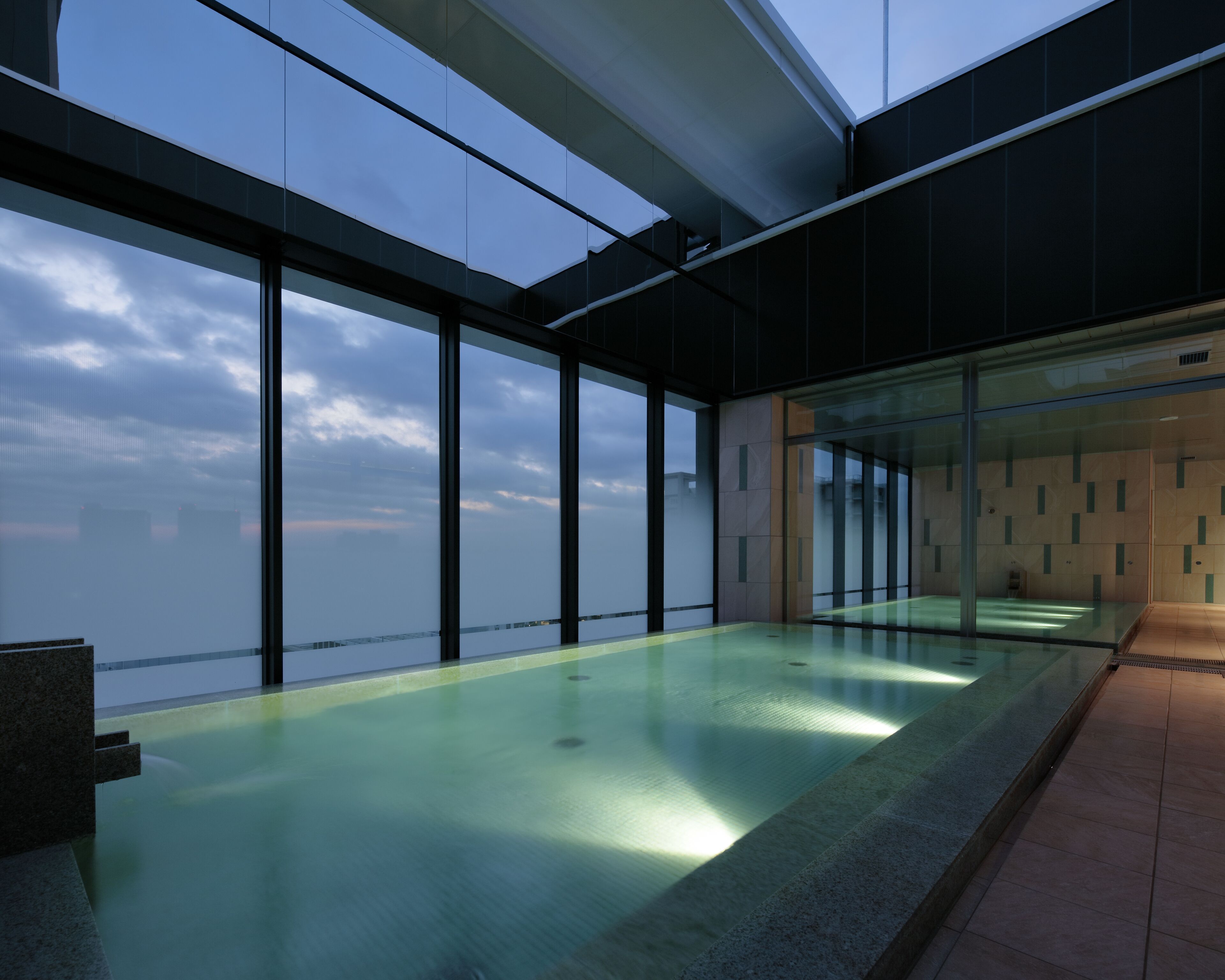 Piscina interior moderna con ventanas amplias y vista al cielo.