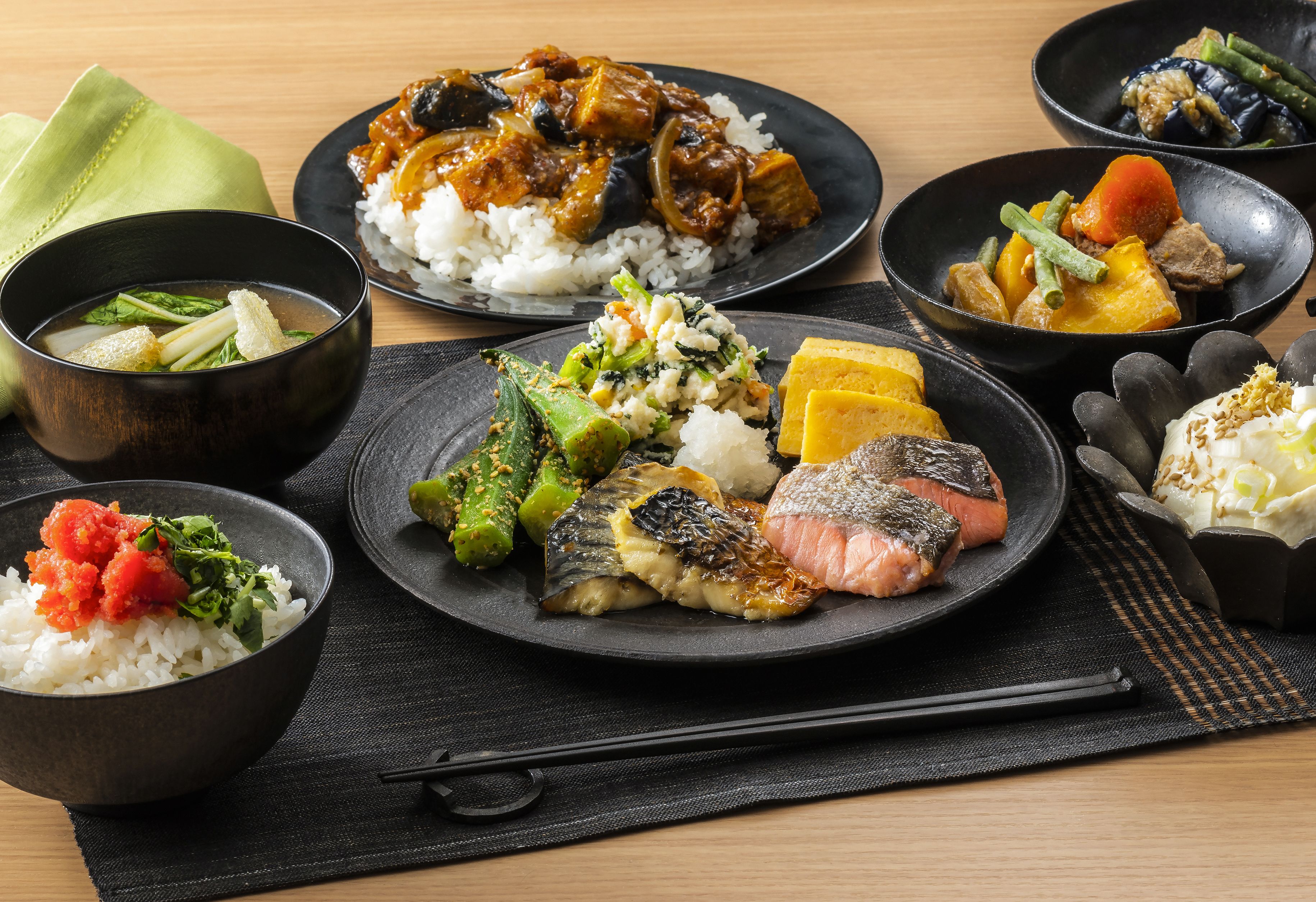 A variety of Japanese dishes including rice, fish, and vegetables on black plates.