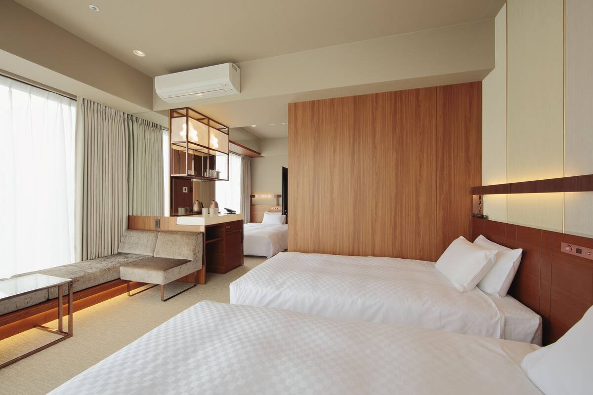 A hotel room with two beds, a sofa, a desk, and a kitchenette.