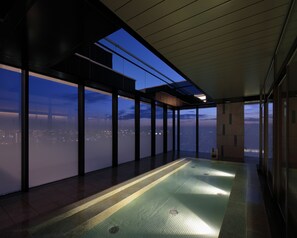 A spacious indoor area with large windows offering a city view at dusk.