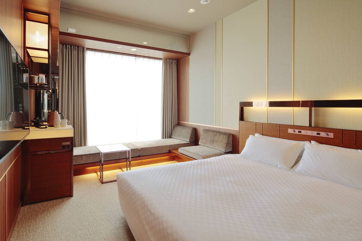 A hotel room with a large bed, a desk with a chair, a sofa, and a small table.