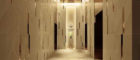 Pasillo de hotel con una columna central, logotipo de estrella y una planta.