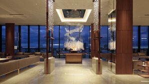 Een moderne lobby met een centraal gelegen receptiebalie, grote ramen met uitzicht op de stad en moderne verlichting.