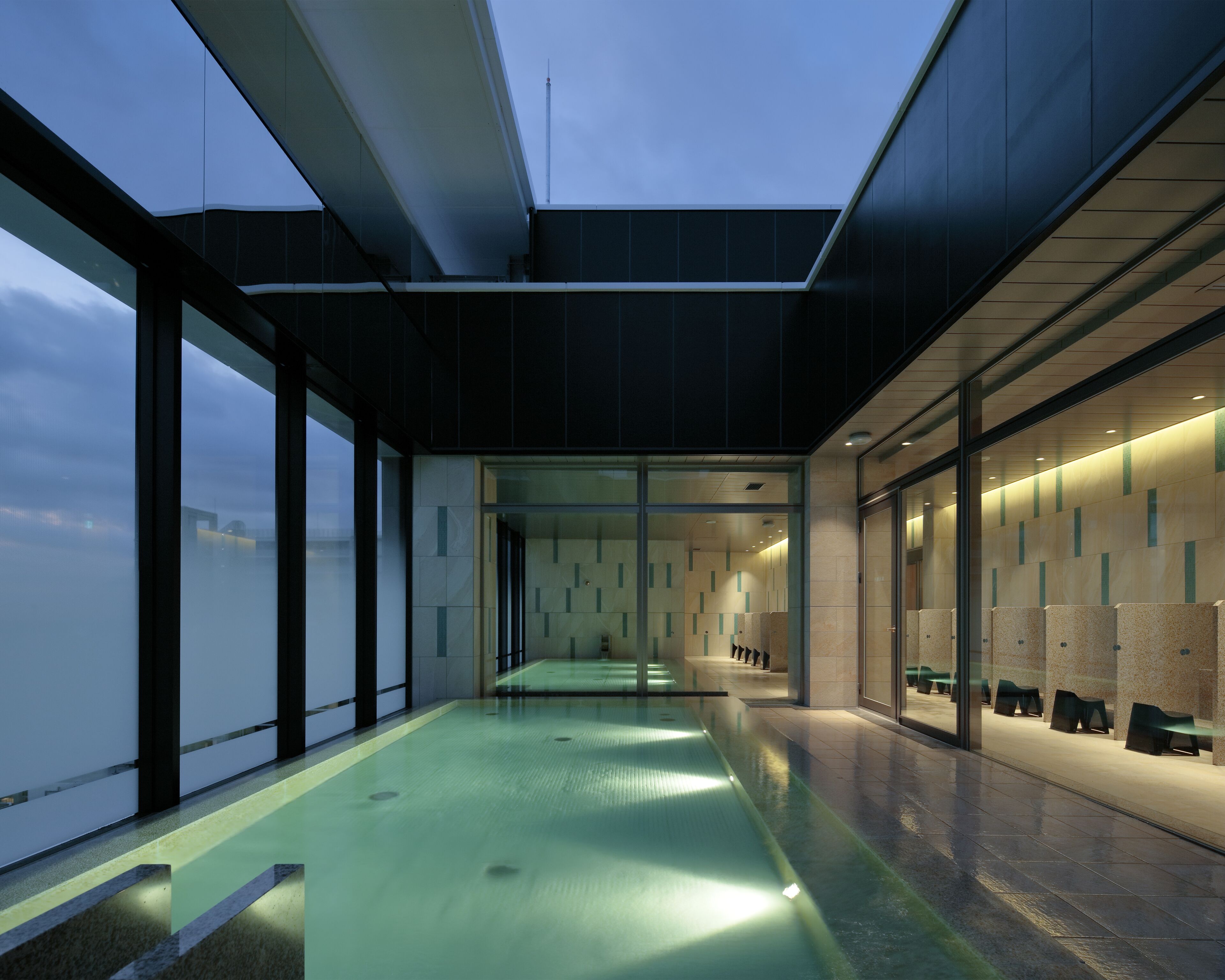 A modern indoor pool area with glass walls, a long pool, and seating along the walls.
