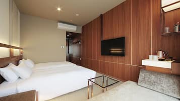 A modern hotel room with a large bed, a flat-screen TV mounted on the wall, a small bedside table, and a built-in vanity with a mirror.