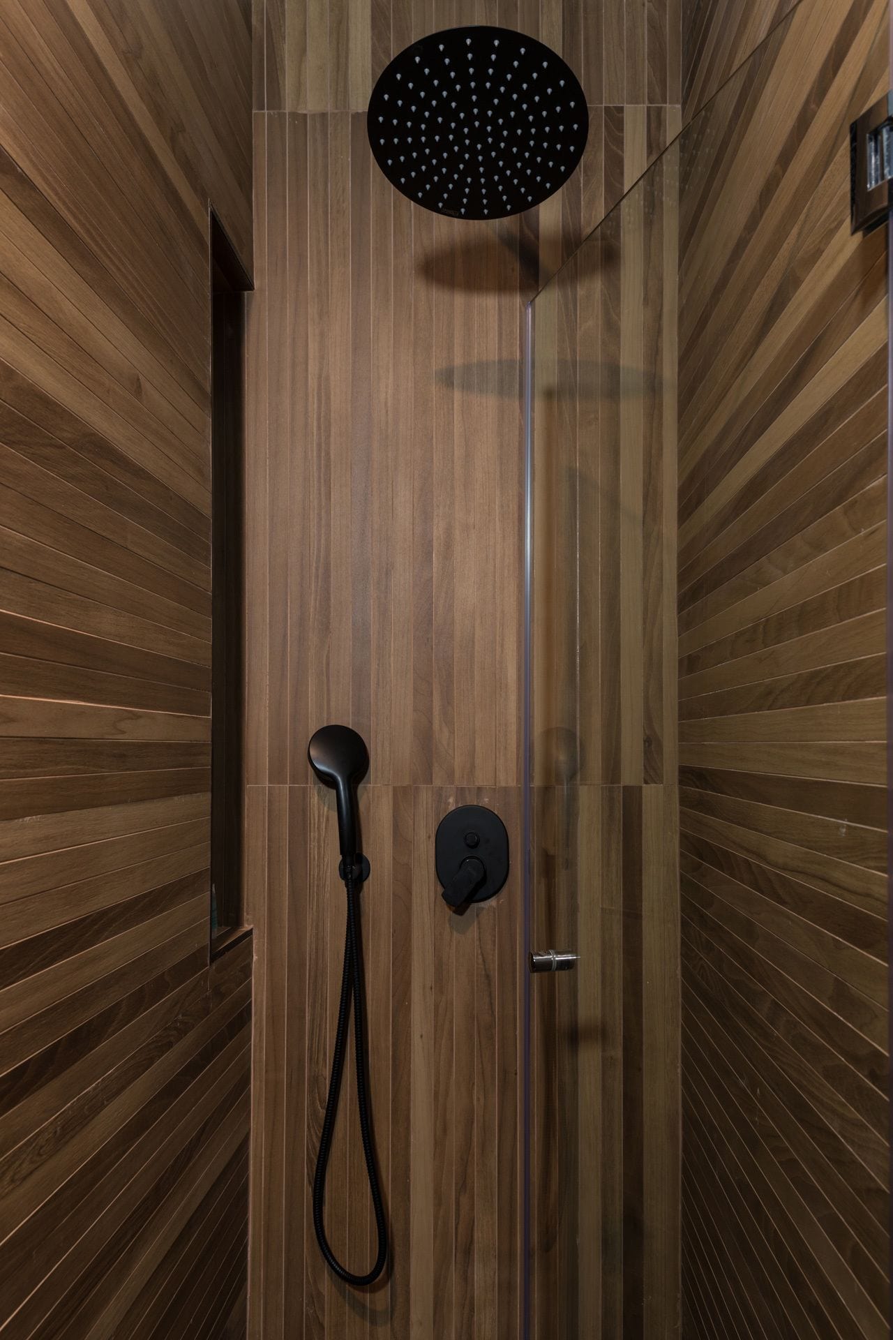 A modern shower enclosure with a wooden panel design, a handheld showerhead, and a control panel.