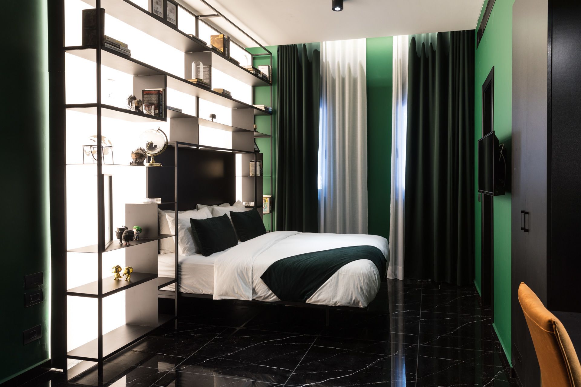 A modern bedroom with a bed, a built-in bookshelf, a flat-screen TV, and a large window with curtains.