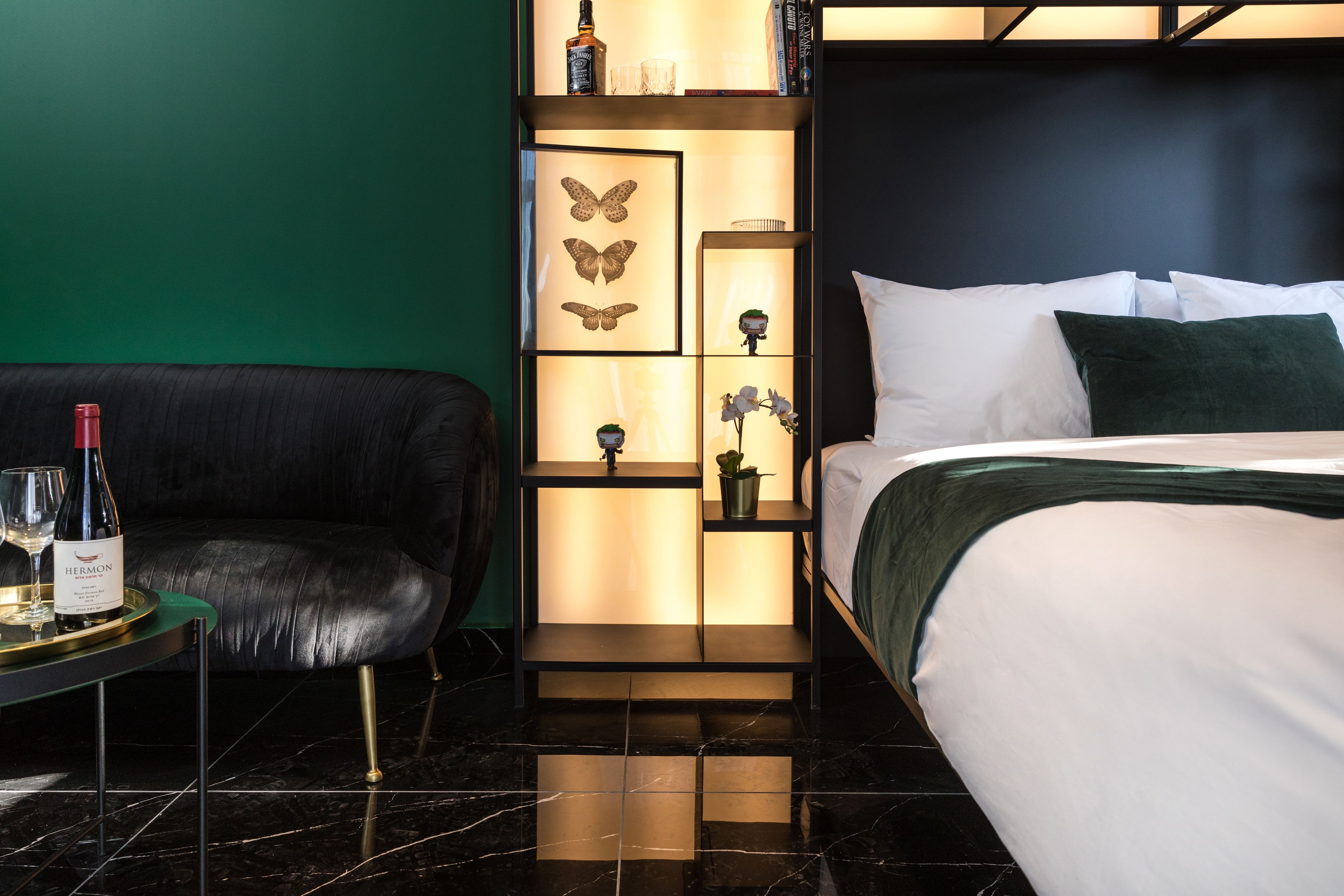 Ein modernes Hotelzimmer mit einer schwarzen Ledersofa, einem Bett mit weißer Bettwäsche, einem Nachttisch mit einer Weinflasche und einer dekorativen Wandverkleidung mit Schmetterlingskunst und Orchideen.