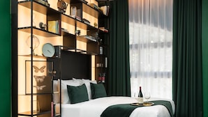 A modern bedroom with a large bed, a built-in bookshelf, and a large window with curtains. - Joseph Hotel TLV (Tel Aviv)