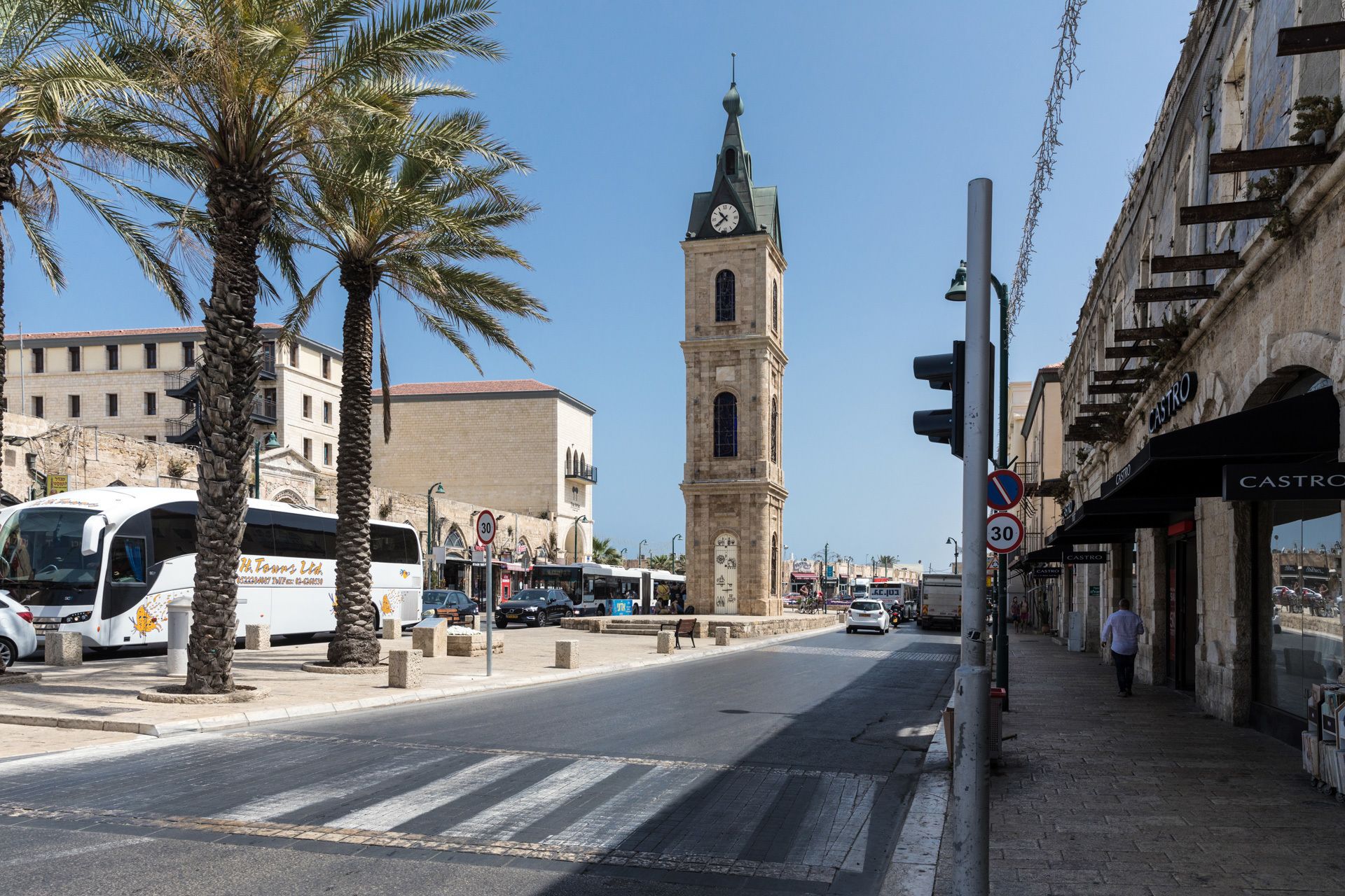Un carrer amb una torre de l'ajuntament destacada, palmeres i un edifici amb un rètol que diu "CASTRO".