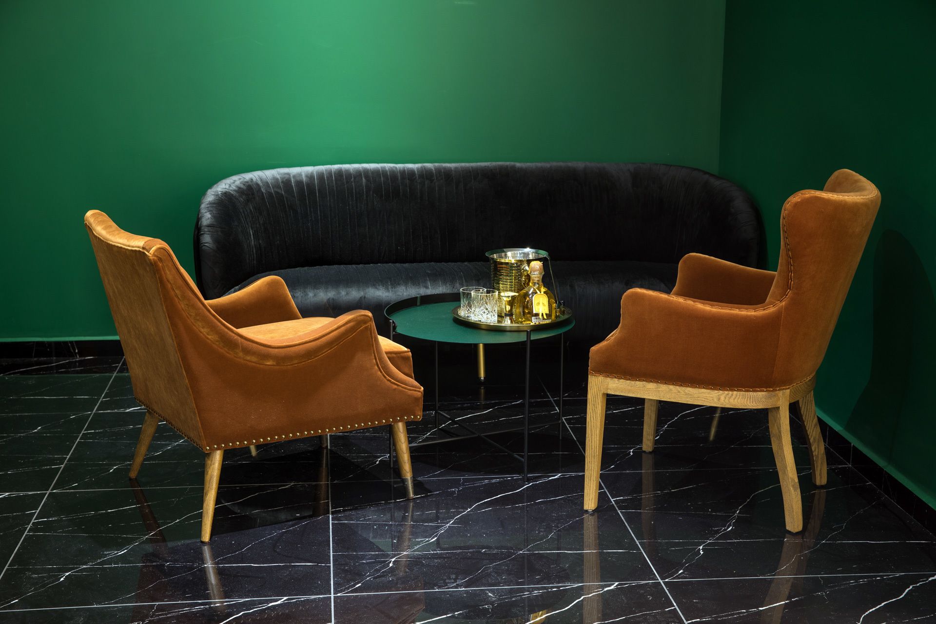 A room with a black leather sofa, two brown leather armchairs, a small round table with a tray, and a green wall.