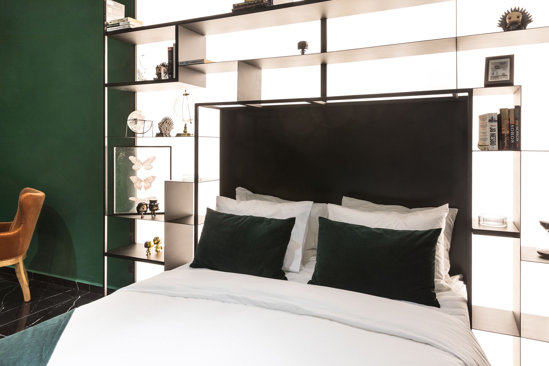 Un dormitorio moderno con una cama grande, una pared de acento verde y estanterías empotradas con adornos.