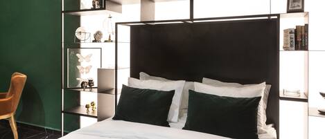 A modern bedroom with a large bed, a green accent wall, and built-in shelving with decorative items.