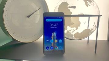 Un teléfono inteligente mostrando la hora y la fecha, un reloj y un globo terráqueo sobre una estantería.