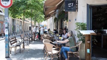 Un café al aire libre con sillas y mesas de mimbre, un letrero que dice 'Deli & Co' y un cartel de 'No estacionar'.