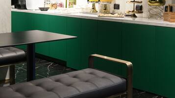 A modern kitchen with green cabinetry, a marble countertop, and a black leather bench.