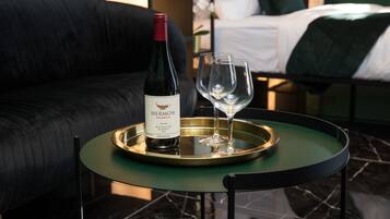 A bottle of Hermon wine on a tray with two glasses on a small round table in a room with a bed and a dark-colored sofa.