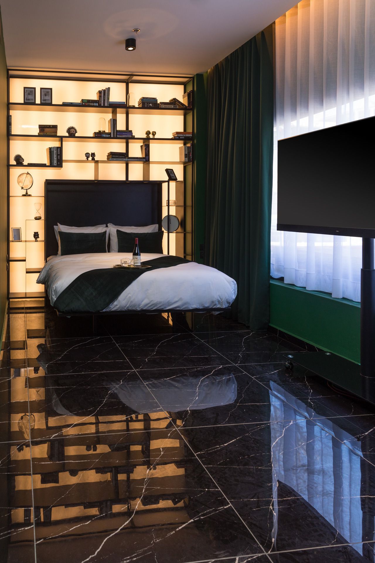 A modern bedroom with a large bed, a flat-screen TV, and a bookshelf.