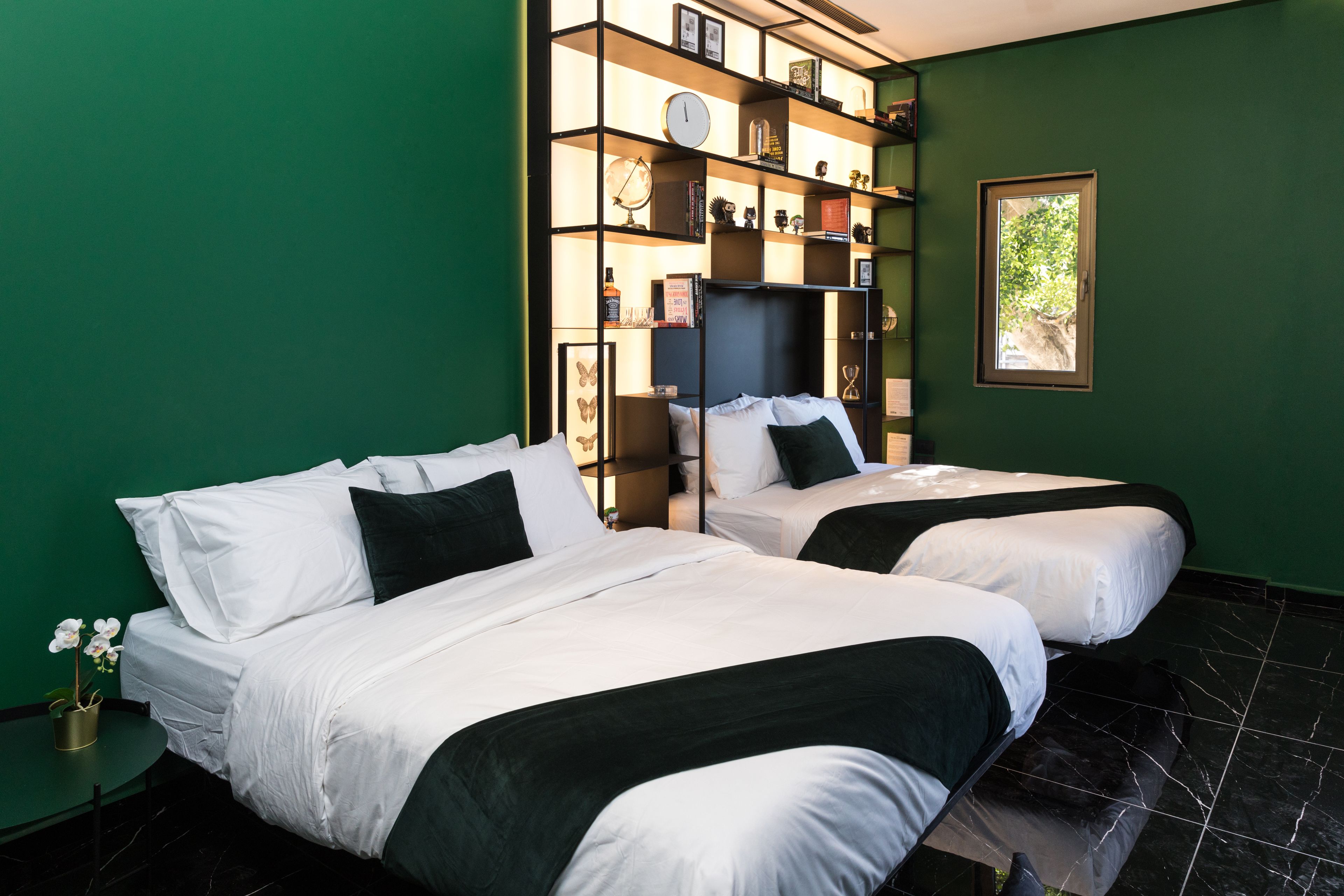 Een hotelkamer met twee bedden, een boekenplank, een klok en een raam.
