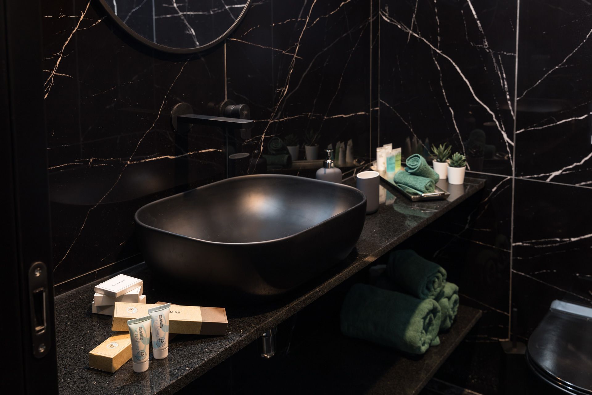 Een moderne badkamer met een grote zwarte wastafel, een spiegel en een plank met toiletartikelen.