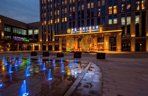 A modern building with a large entrance and a fountain with illuminated jets in the foreground. - CIMC Executive Apartments (Yangzhou)