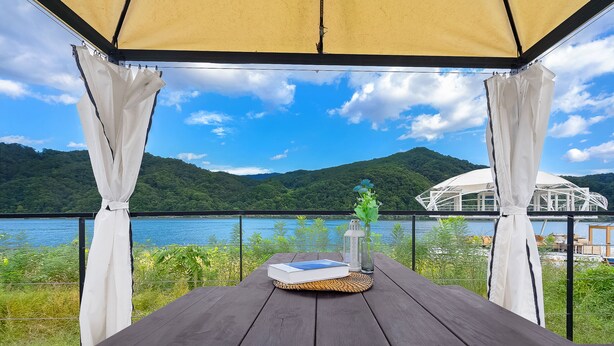 Una terraza de madera con una mesa para dos, con vista a un lago y montañas.