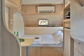 A compact room with a bed, a small table with bottles, a television, and a microwave. - Poseidon Caravan - Campsite (Gapyeong)
