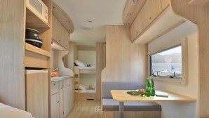 Interior compacto de una autocaravana con kitchenette, comedor y litera.