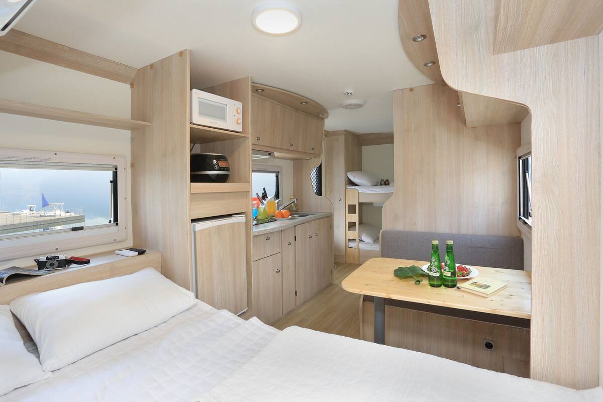 A compact RV interior with a bed, kitchenette, and seating area.