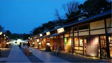 Une rue traditionnelle japonaise au crépuscule, avec des bâtiments en bois et des enseignes illuminées.