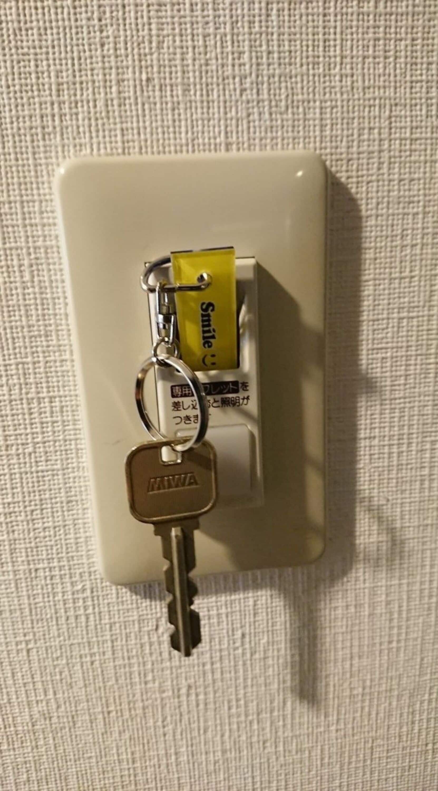 A white electrical outlet with a yellow battery and two keys attached to it.
