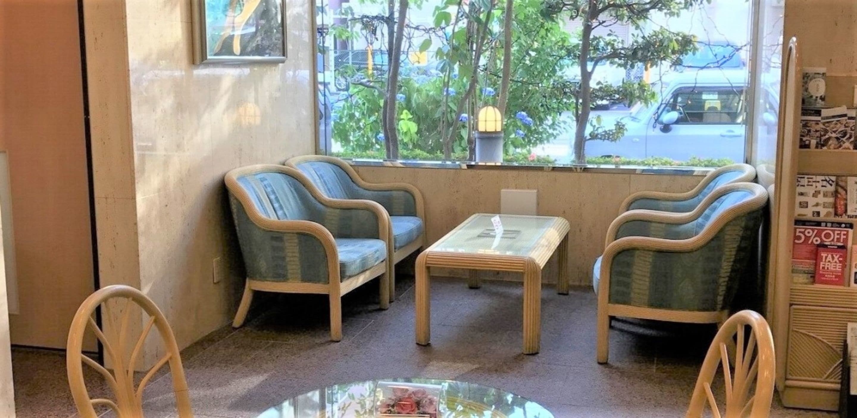 Un área de descanso con dos sillas y una mesita, una ventana que da a la calle y una máquina expendedora con un cartel de 5% de descuento.