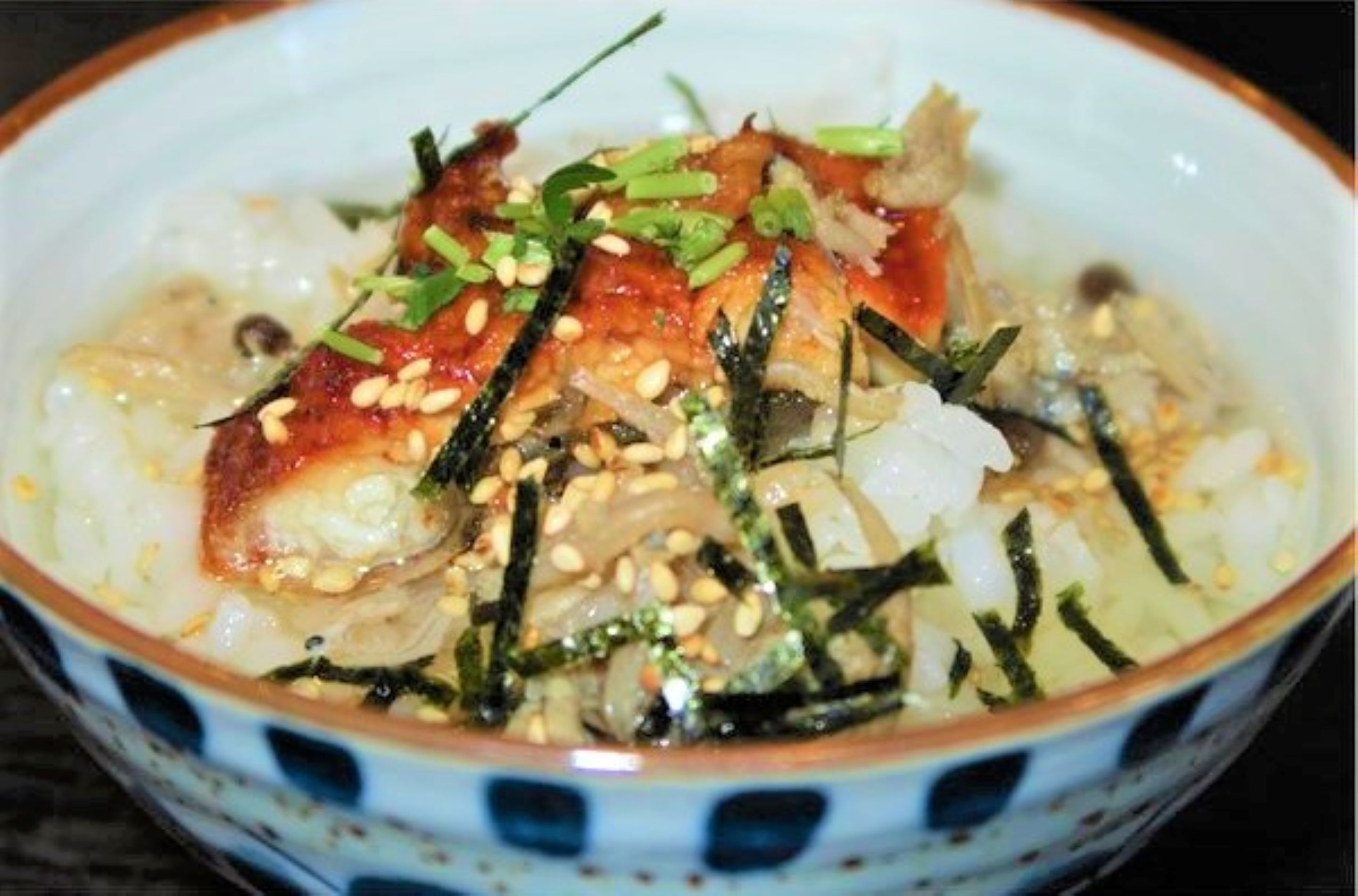 A bowl of food with rice, fish, and garnishes.