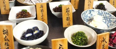 Variedad de platos japoneses con etiquetas de madera, incluyendo vegetales encurtidos, dumplings y un tazón de arroz.