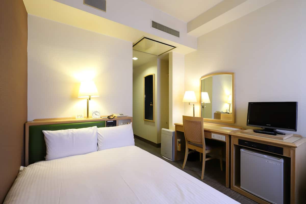 A hotel room with a bed, desk, chair, television, and a small refrigerator.