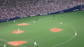 Un estadio de béisbol con varios jugadores en el campo, público en las gradas y anuncios en las paredes.
