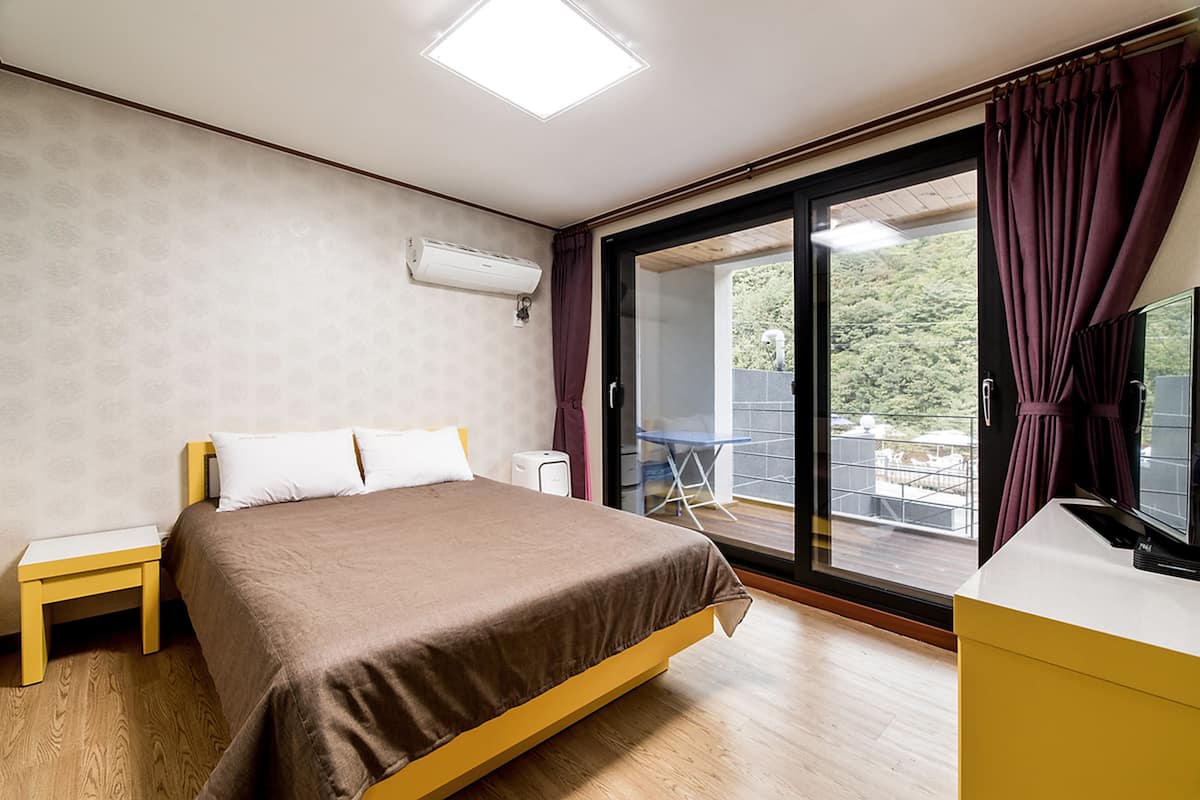 A bedroom with a bed, a nightstand, a desk, and a window with curtains.