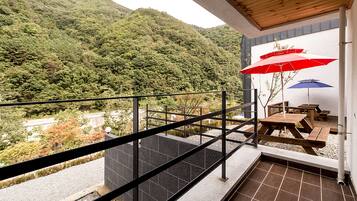 A balcony with a view of a forested hillside, a wooden table, and two umbrellas.