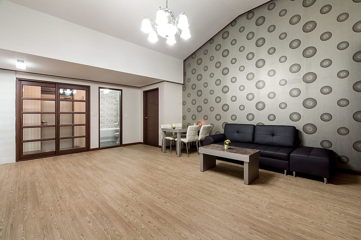 A spacious living room with a wooden floor, a dark sofa, a coffee table, and a patterned wallpaper.