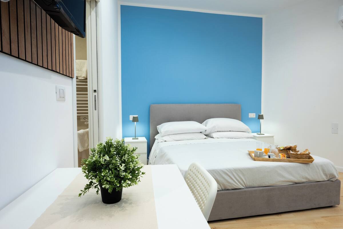 A modern bedroom with a bed, bedside tables, a potted plant, and a breakfast tray.