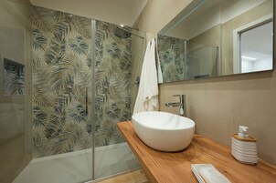 Un baño moderno con cabina de ducha de vidrio, lavamanos blanco y tocador de madera.