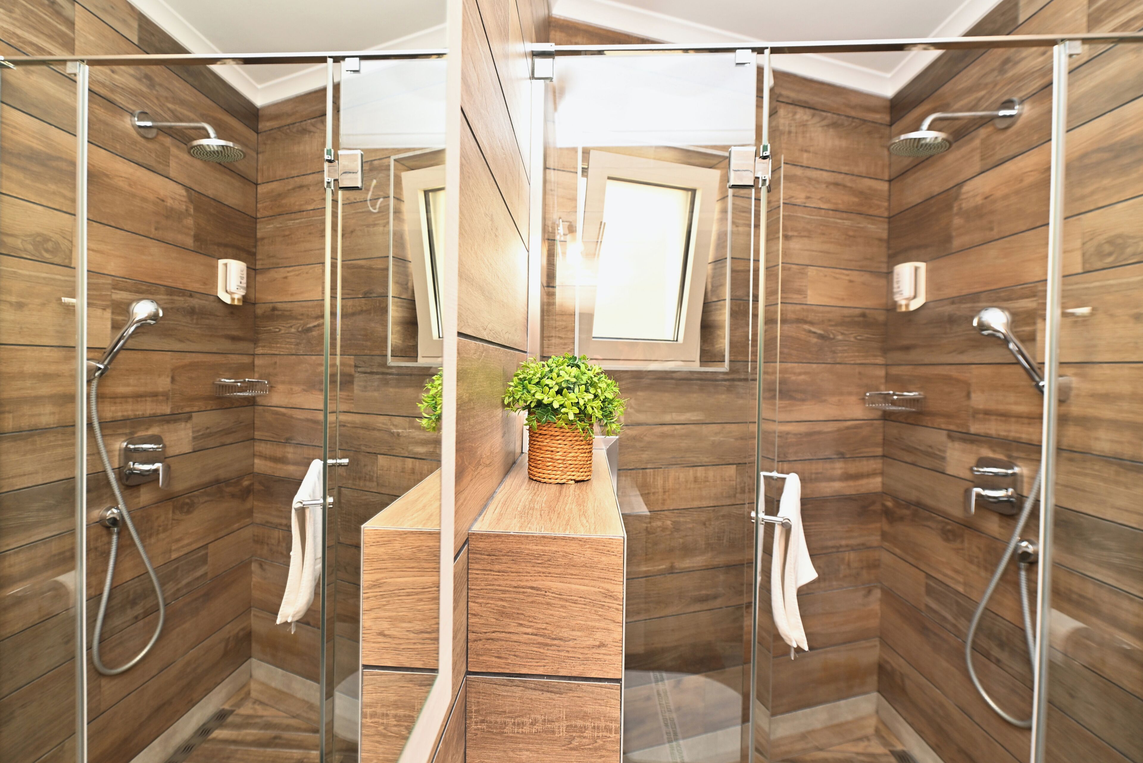 A modern bathroom with wooden paneling, a glass shower enclosure, and a small plant on a wooden shelf.