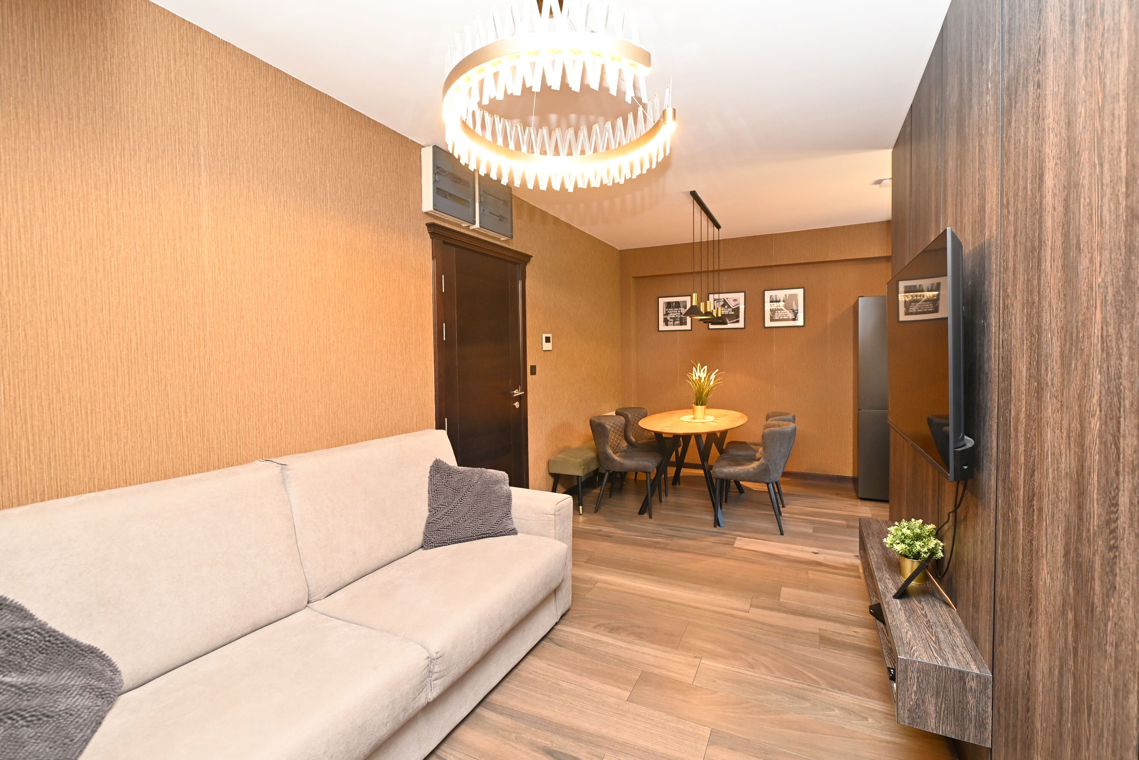 Una sala moderna con un sofá, una mesa de comedor con sillas, una araña y un televisor montado.
