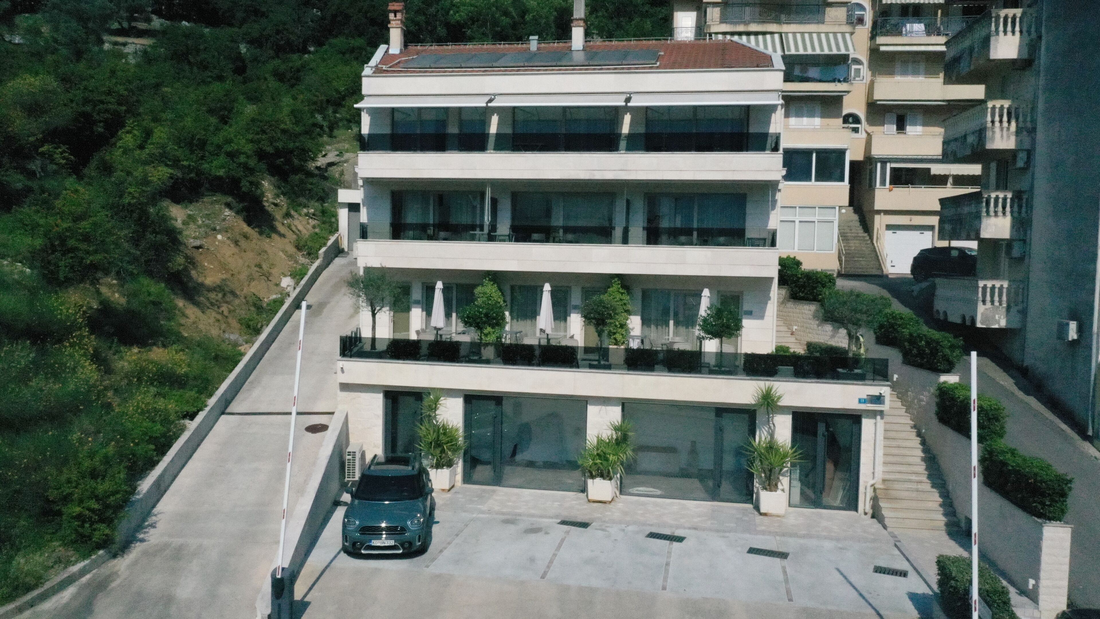 Un immeuble à plusieurs étages, doté d’un toit plat, de grandes fenêtres et d’un espace de stationnement où se trouve une voiture.