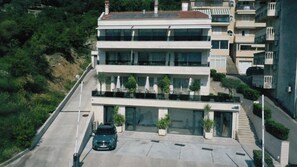 A multi-story building with a flat roof, large windows, and a parking area with a car. - Casa Nuova (Kotor)