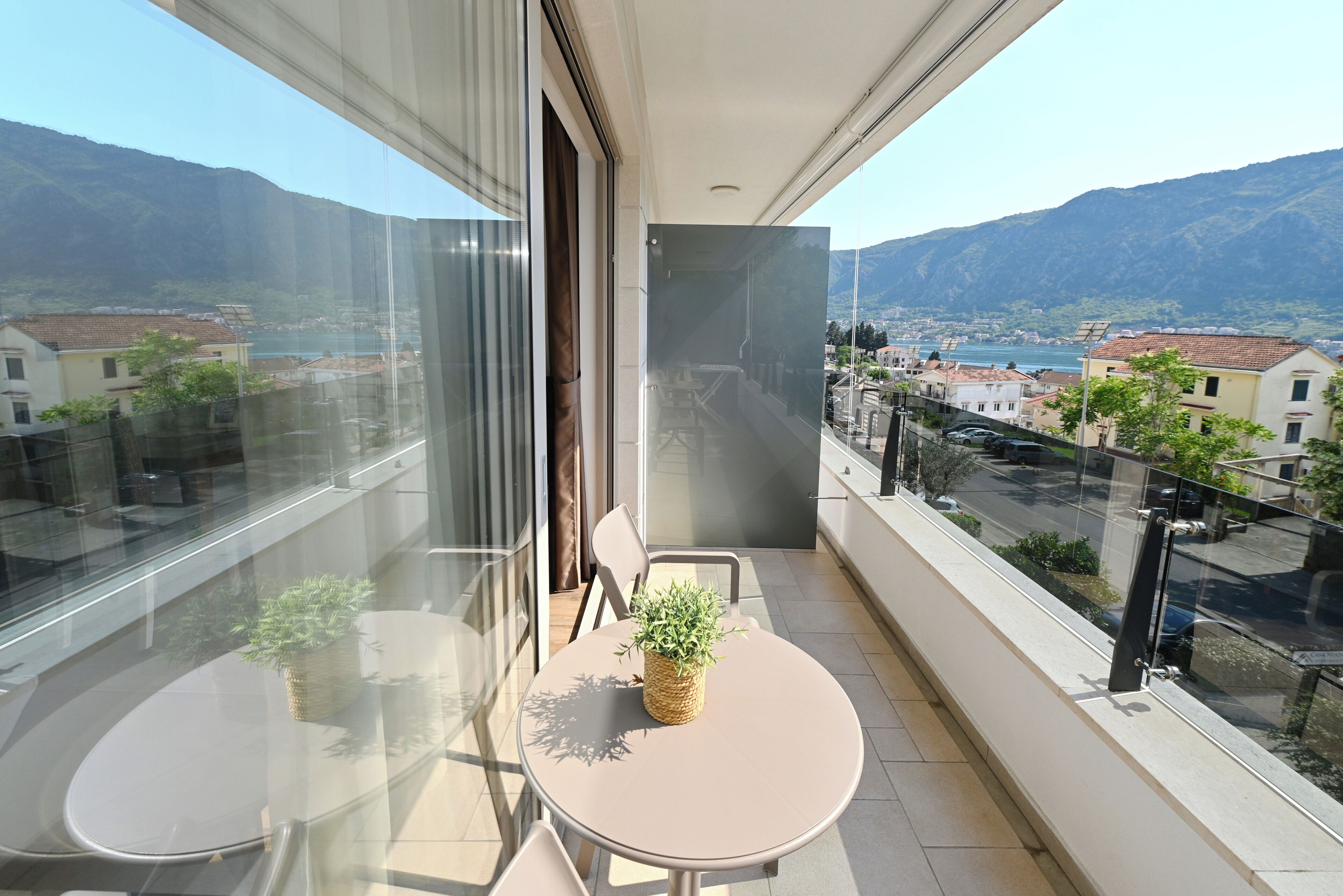 A balcony with a table and chairs, a potted plant, and a view of a town and mountains.