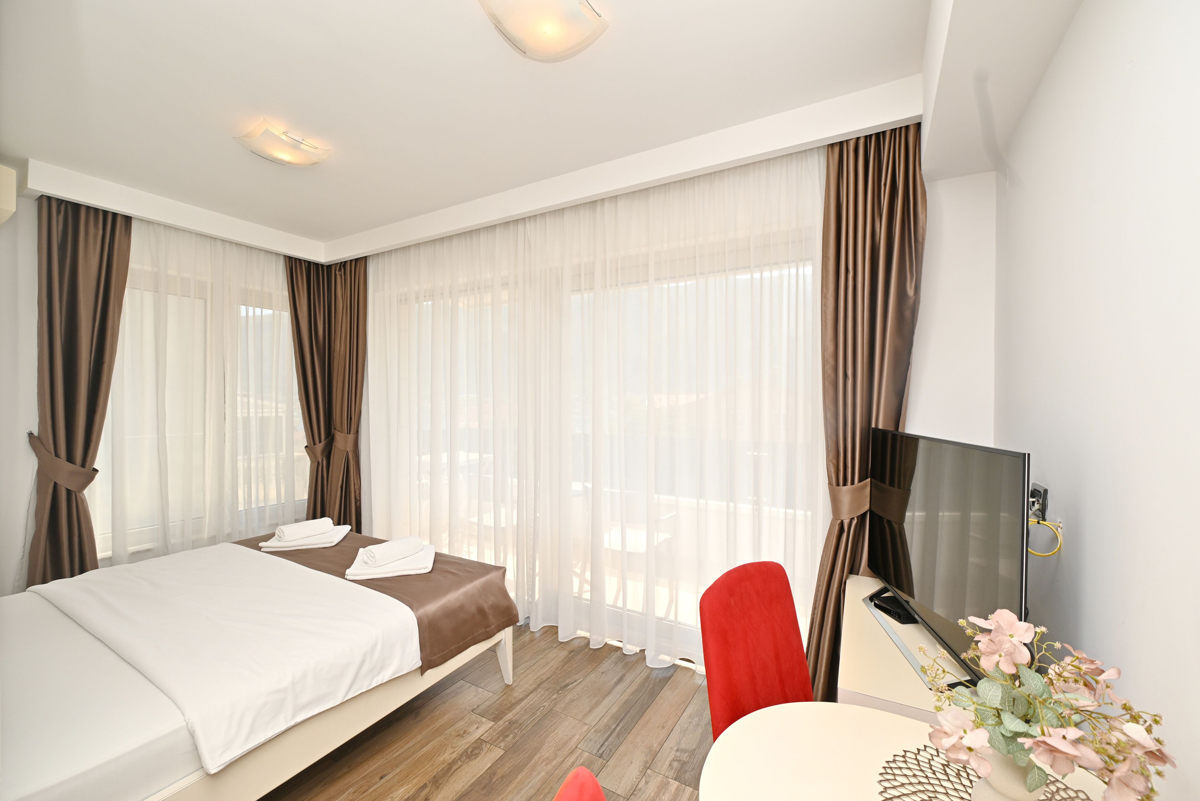 Una habitación de hotel con una cama, un escritorio con televisor y una ventana con cortinas.