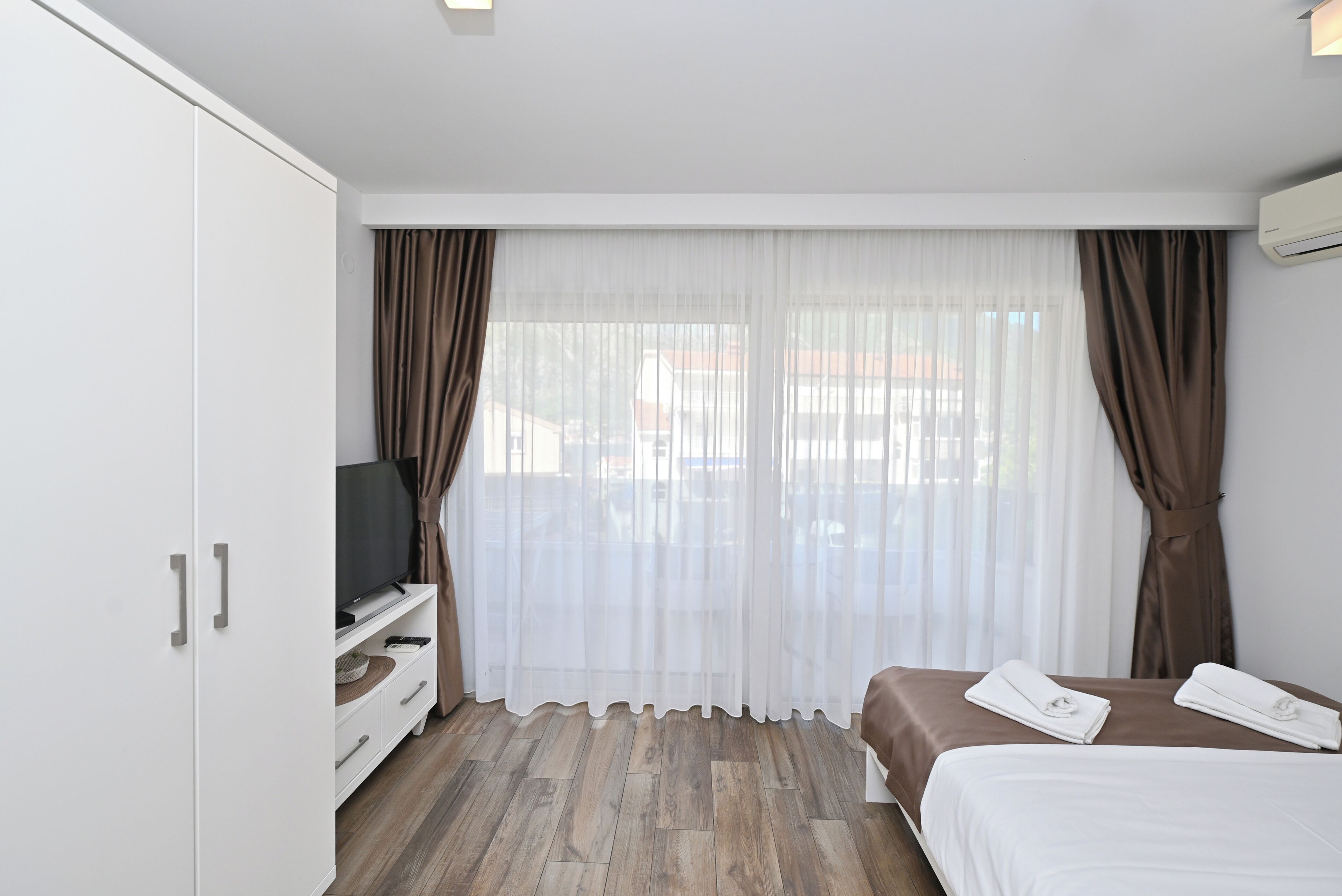 A hotel room with a bed, a TV on a stand, a wardrobe, and a window with curtains.